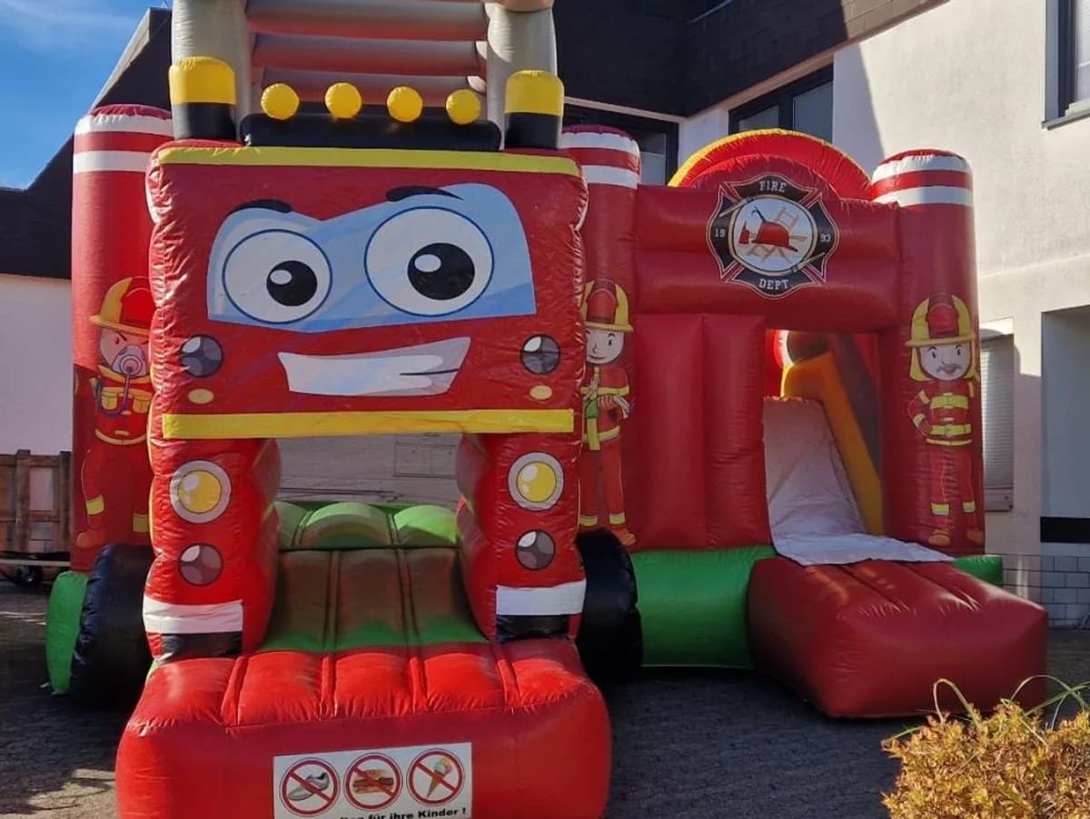 Hüpfburg im Feuerwehr-Design mit Comicgesicht und Rutsche