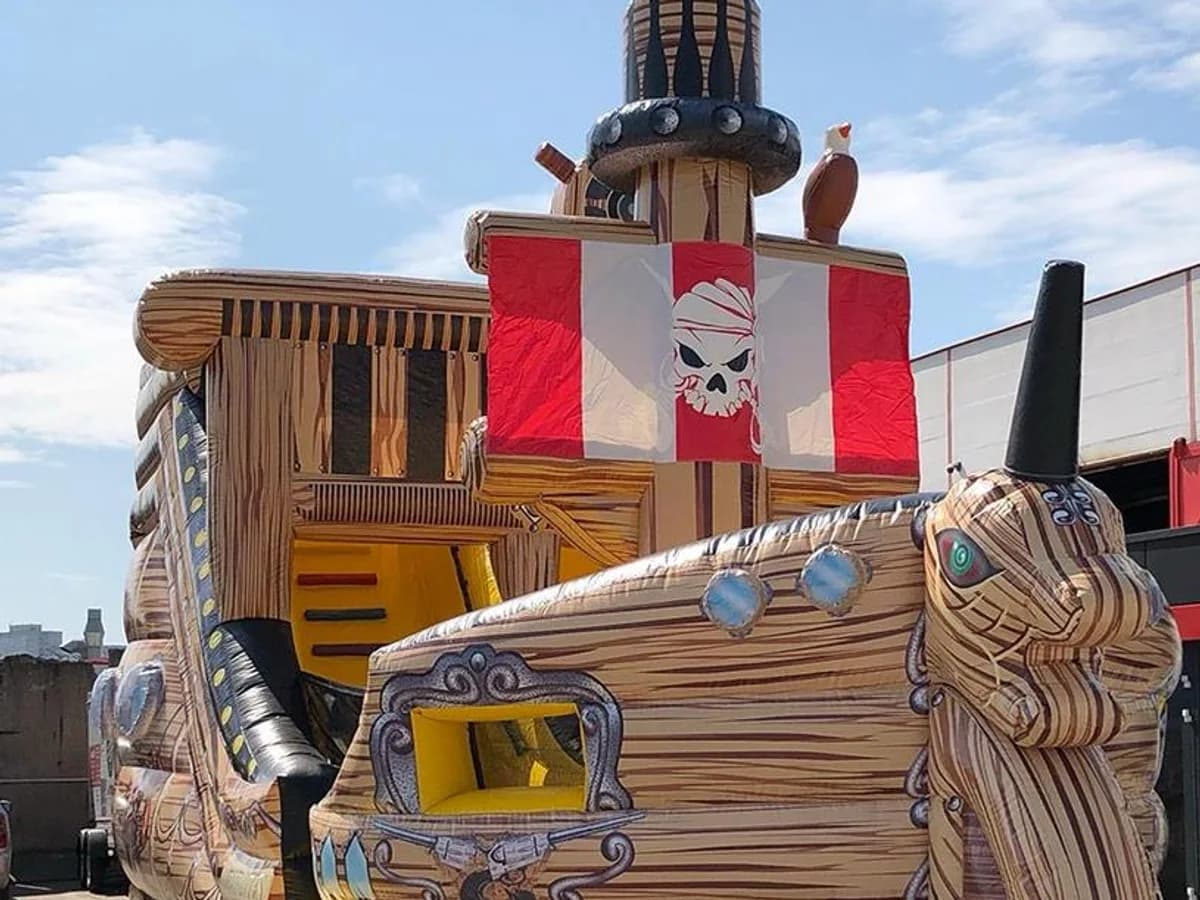 Piratenschiff-Hüpfburg in Holzoptik mit Totenkopf-Flagge und Galionsfigur